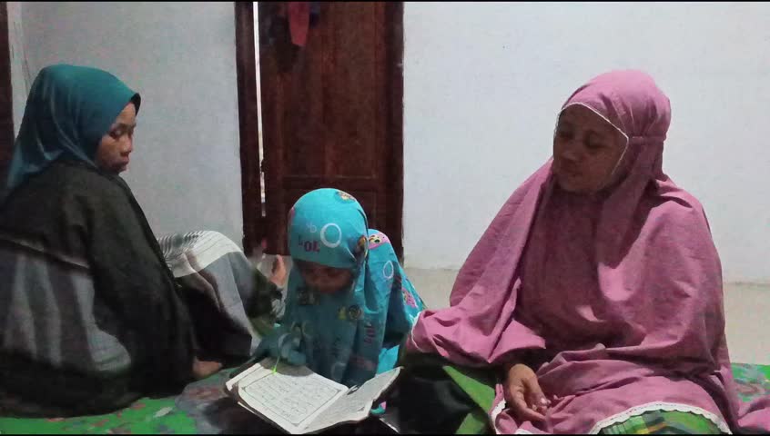 Little girl learning Arabic letters from Iqra book with mother and grandmother. Authentic Indonesian Muslim family daily life scene.