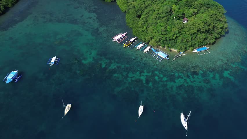 Aerial top down drone view of small boats floating in a tropical bay in Puerto Galera Philippines featuring crystal clear turquoise water, calm sea and vibrant colors ideal for travel and diving.