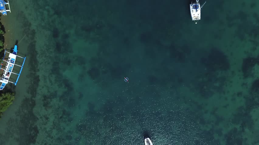 Aerial top down drone view of small boats floating in a tropical bay in Puerto Galera Philippines featuring crystal clear turquoise water, calm sea and vibrant colors ideal for travel and diving.