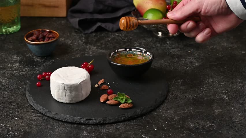 A man prepares dessert. Camembert cheese with honey, cranberries and almonds. A delicious homemade dessert. Panning camera.