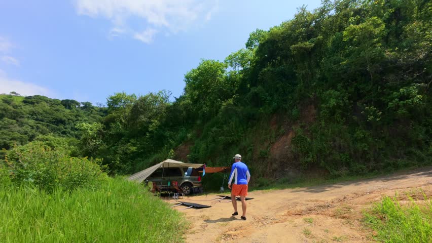 Man places foldable solar panels under sun at overlanding camp in Mexico. Panoramic static view