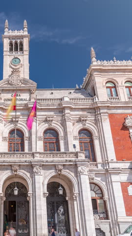 The town hall facade with flags in Plaza Mayor timelapse, Valladolid. Blue sky and historic architecture in the heart of the city. Pedestrians pass by in this central square.