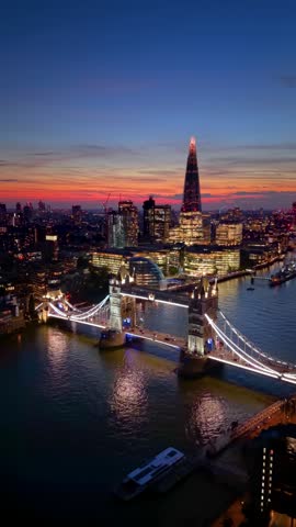 Aerial view of the illuminated Tower Bridge, River Thames and City skyscrapers in London, England, during dusk twilight