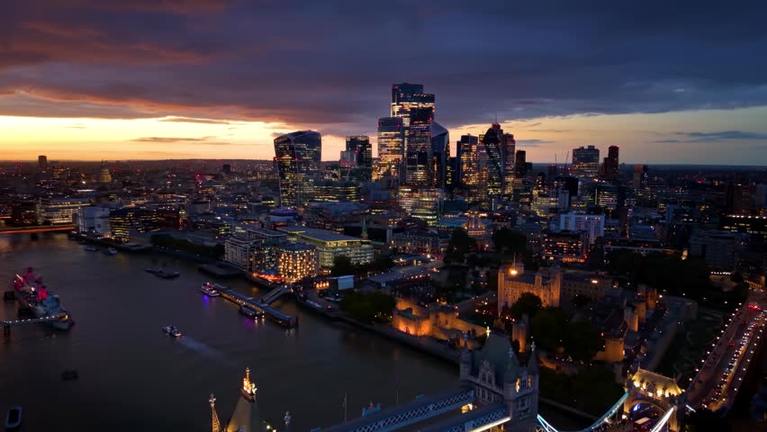 Aerial hyperlapse view of the illuminated London, England, skyline with Tower Bridge, City skyscrapers and river traffic during dusk