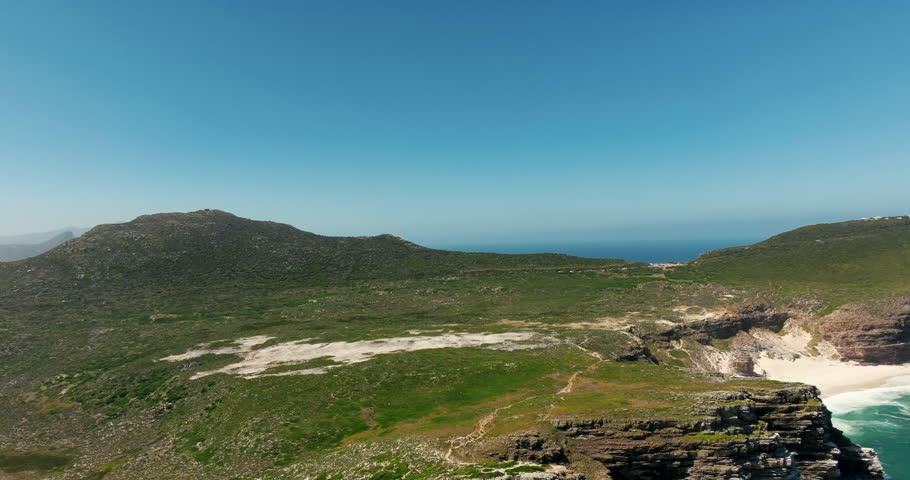 Aerial footage of the Cape of Good Hope in South Africa showing vibrant green landscape, a bright lagoon, rugged mountains, and clear sunny weather. Ideal for travel, nature and documentary projects