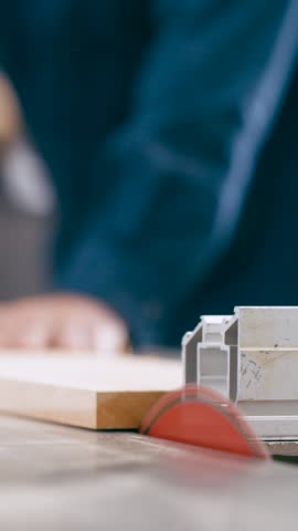 Close up view of a professional carpenter using a circular table saw to cut a wooden plank. Sawdust flies as the sharp blade slices through the timber. Vertical