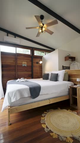 Comfortable and stylish bedroom interior with wooden walls and flooring. A large bed with white linens and a rotating ceiling fan