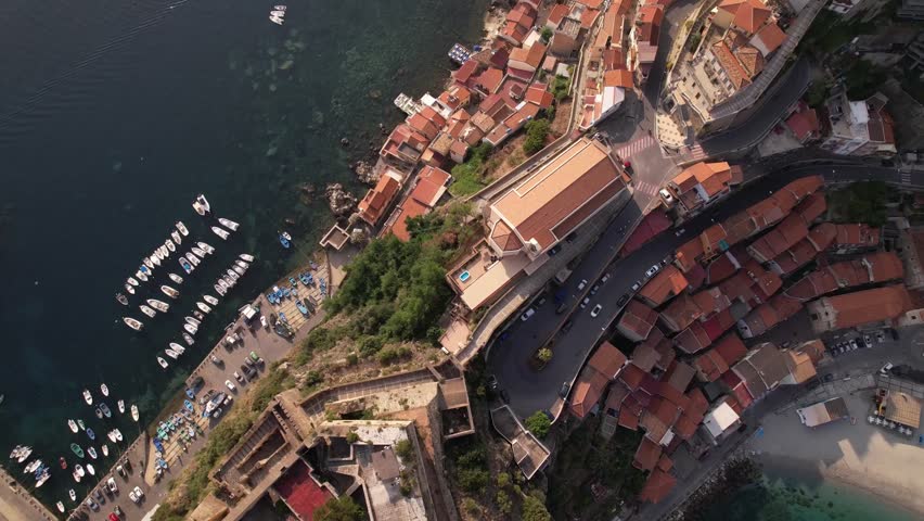 Aerial view of coastal beach town with buildings, boats, and clear blue water.
