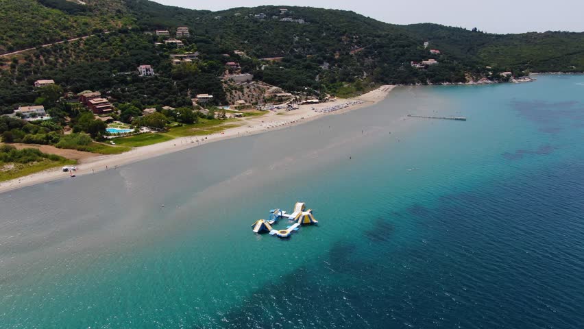 Aerial view of an inflatable floating water park playground in the shallow turquoise sea at a sandy beach in North Corfu Greece summer fun and water sports for kids