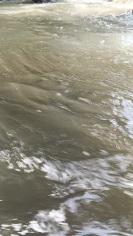 Rushing river stream close up. Rapid water flow over rocks creates white foam and ripples.