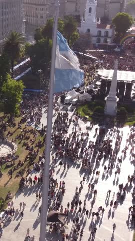 A high angle view capturing the motion of the argentinian flag waving in the wind above a bustling public square during an event