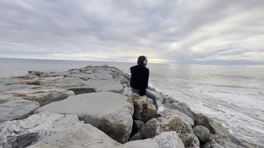 Teenager girl in yellow jacket sitting on a rock and looking at stunning nature background with ocean and cliffs. Travel and tourism. portugal. Dramatic sunset sky. Famous area.