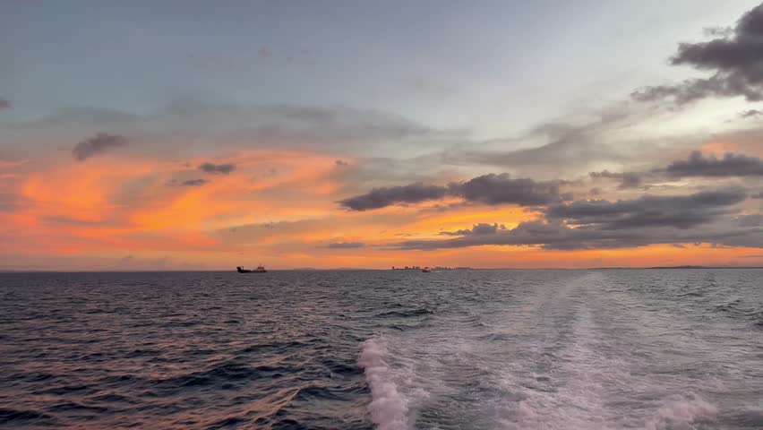 Vibrant orange yellow sunset over sea with boat wake in foreground, dark clouds and peaceful ocean seascape. 
