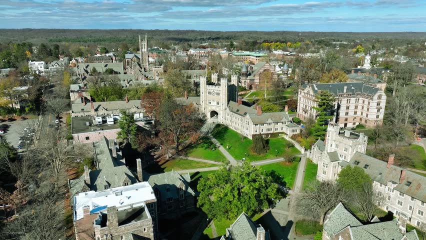 Aerial view of Princeton University campus and the surrounding town in New Jersey, showcasing iconic ivy-covered academic buildings, green courtyards, and historic streets.