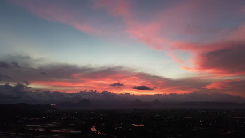 Cinematic aerial footage of dramatic sunrise sky with red and orange clouds over dark rural landscape. Vibrant colors, moody atmosphere, and wide horizon create a powerful cinematic background for travel, nature, and creative projects.