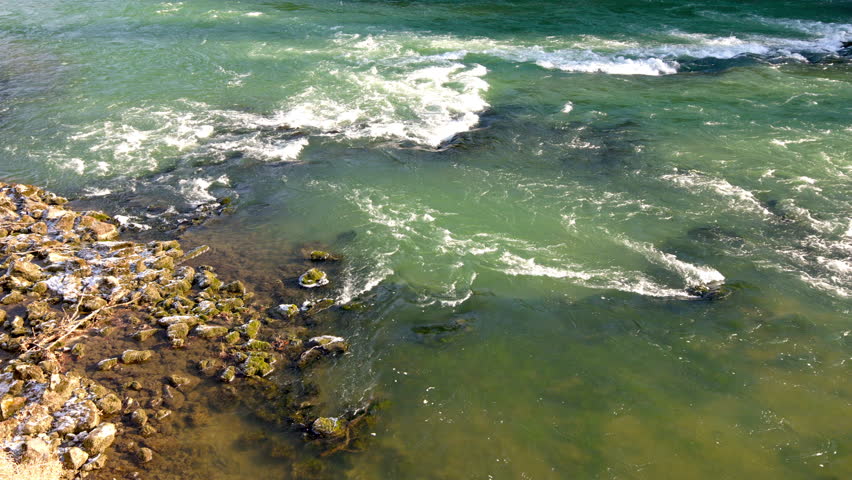 Wild river winter footage with fast-flowing green water and visible currents. Cold season river scene with rocks along the shore, subtle snow traces, natural outdoor motion background