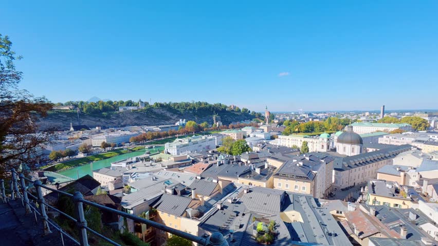 SALZBURG, AUSTRIA – OCTOBER 3, 2025: A high-angle panoramic view of the city featuring traditional rooftops, church spires, and historical architecture under a clear blue sky. The shot captures the urban landscape of the old town area extending toward the distant horizon.