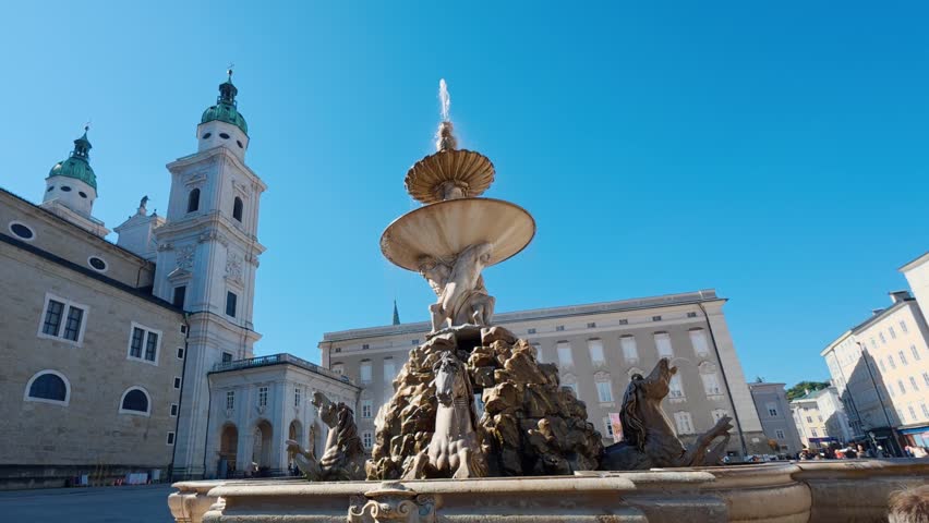 SALZBURG, AUSTRIA – OCTOBER 3, 2025: A camera orbits the Residenzbrunnen, a monumental Baroque fountain featuring marble horse sculptures and mythological figures. The video captures the intricate details of the landmark located in the center of Residenzplatz under a clear sky.