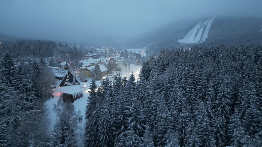 Aerial View Of Snowy Slopes And Trees with a small city of Harrachov in Czech Republic