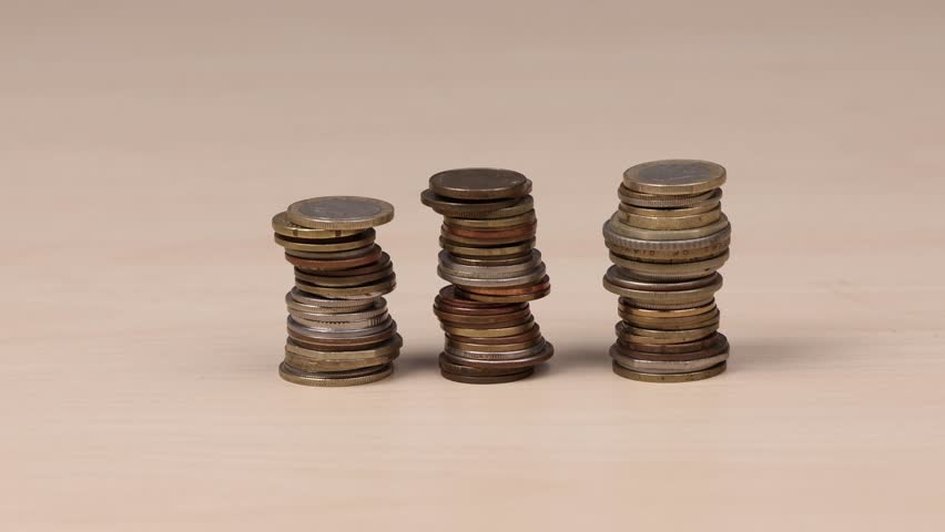 Stacks of coins collapsing and falling on wooden table