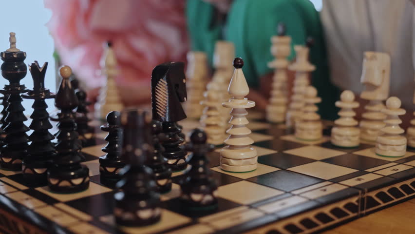 ornate chessboard, carved chess, chessboard macro. Close-up ornate chessboard with unique carved pieces as children observe game, emphasizing focus and strategy.