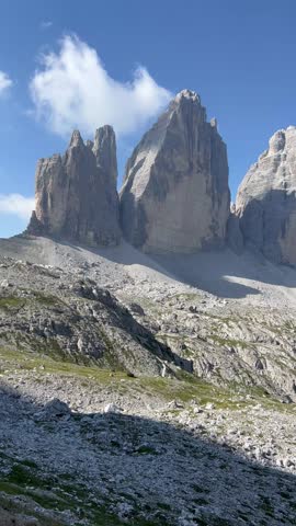 South Tyrol, Italy - July 25 2022: The famous Italian national park Tre Cime di Lavaredo. Horse racing in the Dolomites. Mountain lake. The rocky landscape of the Dolomites is characterized by inaccessible terrain with scattered boulders and a small reflective mountain lake. A winding path runs through patches of green among the rocky surface. In the background, jagged mountain peaks under a partially cloudy sky create a dramatic panorama of the Alps. The scene captures the pristine beauty and appeal of this famous Italian region. 