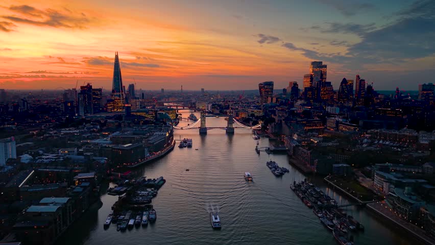 Panoramic aerial sunset view towards the Tower Bridge in London, England, with city skyline and river Thames in the background
