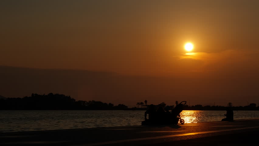 People sitting on bay against sunset. A view of people silhouette resting on bay by the lake against bright evening sky