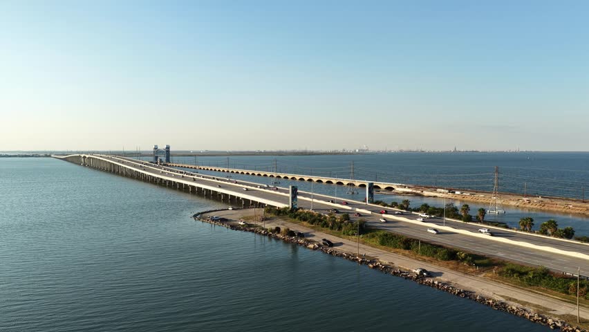 Houston, Texas, United States – November 2025.
Aerial drone footage of a long highway bridge crossing open water in Houston, showing steady vehicle traffic moving in both directions. The drone maintains a high, wide perspective while slowly advancing forward, highlighting the scale of the bridge infrastructure, surrounding shoreline, and calm water surface under clear daytime skies. Editorial use only.