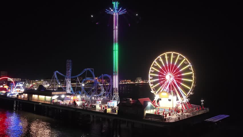 Houston, Texas, United States, USA, November 2025, night, nighttime, amusement park, amusement pier, pier, waterfront, coastline, Gulf Coast, Ferris wheel, roller coaster, thrill ride, fairground, carnival rides, entertainment, leisure, tourism, travel destination, city lights, neon lights, LED lights, reflections, water reflections, sea, ocean, urban nightlife, coastal city, public attraction, infrastructure, landmark, recreation, aerial view, drone footage, wide shot, night lights, outdoor entertainment, editorial