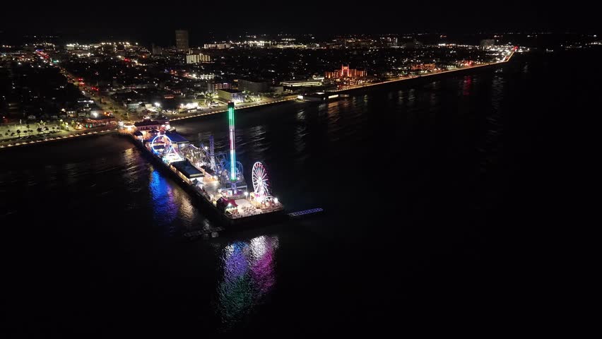 Galveston Island, Texas, United States – November 2024:
Aerial drone video capturing the Galveston Pleasure Pier illuminated at night, featuring colorful lights, amusement rides, and waterfront structures. The footage showcases the pier as a landmark leisure destination along the Gulf Coast.