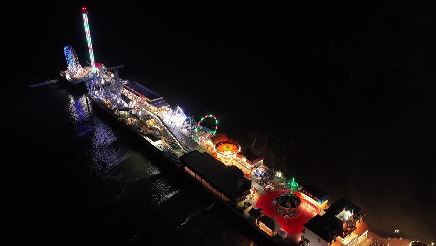 Galveston Island, Texas, United States – November 2024:
Aerial nighttime shot of the Galveston Pleasure Pier captured by drone, showcasing the Ferris wheel, roller coaster, and vertical tower ride illuminated against the coastal skyline of Texas.