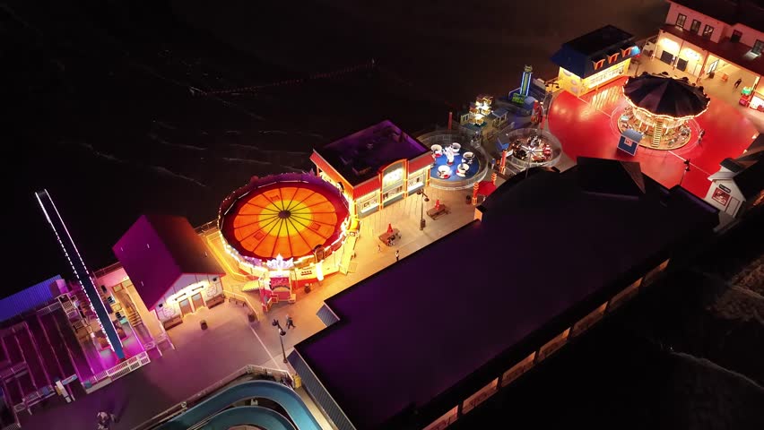 Galveston Island, Texas, United States – November 2024:
Drone view at night of the Galveston Island Pleasure Pier highlighting the Ferris wheel glowing in blue lights and the surrounding amusement rides over the water. The video conveys the vibrant nightlife of this coastal city.