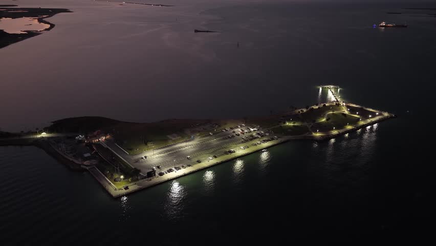 Galveston Island, Texas, United States – November 2024:
Drone video captured at night with a gentle vertical descent, focusing on a waterfront parking lot and nearby shoreline illuminated by artificial lighting.