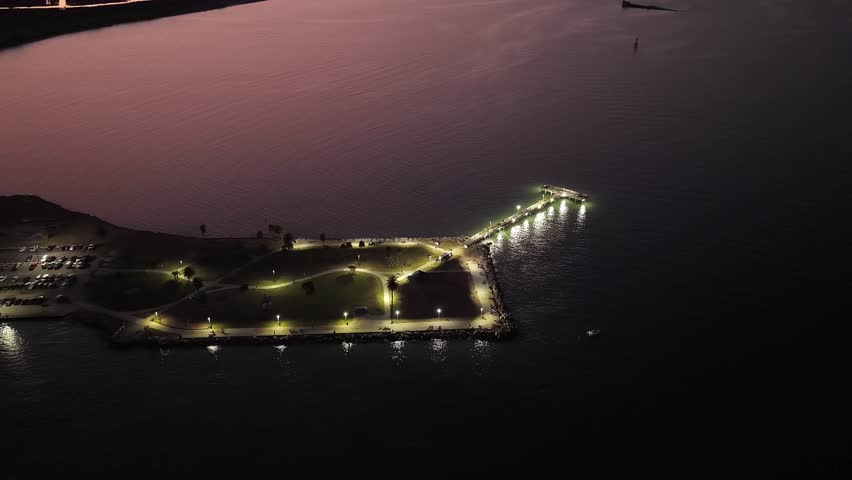 Galveston Island, Texas, United States – November 2024:
Aerial night footage featuring a smooth top-down drone view of a coastal area, highlighting parked cars, marked lanes, and surrounding water under low-light conditions.