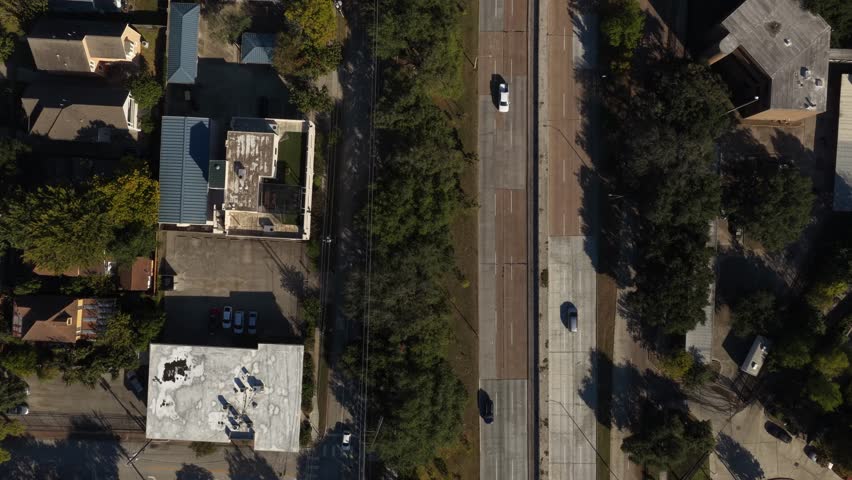 Houston, Texas, United States – November 2025:
Vertical aerial drone shot of a Houston street corridor featuring houses, small buildings, green areas, and steady traffic along a divided road. The overhead composition documents the relationship between residential zones and transportation routes within the city.