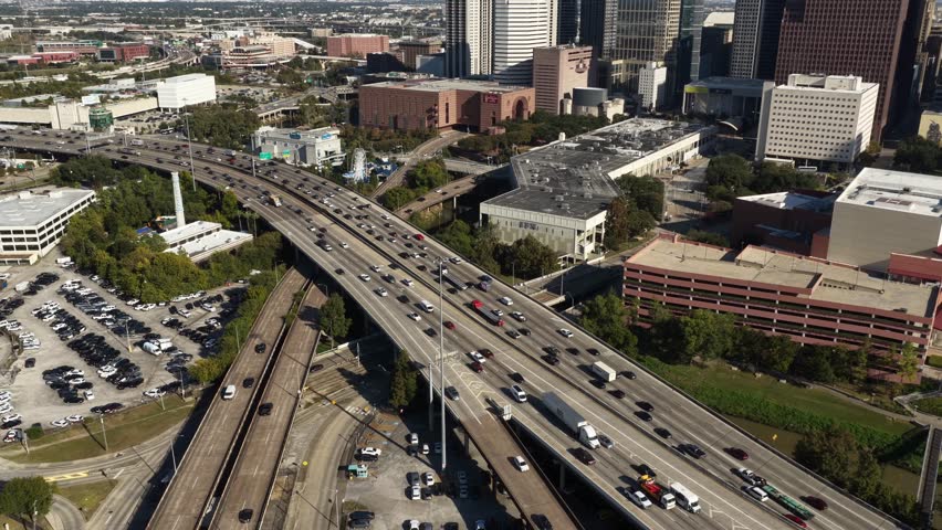 Overhead aerial shot of a central highway corridor in Houston, Texas, USA, recorded in November 2025. Continuous traffic streams run alongside residential zones and office complexes, emphasizing the scale of urban planning and daily commuter movement.