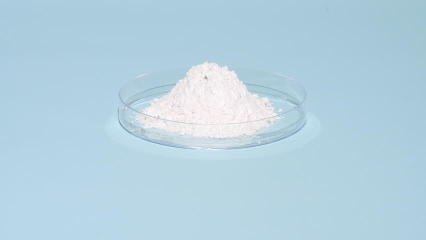 Vertical tracking shot of a stack of white fine powder inside a plastic petri dish on a pale blue background lit with orbiting light casting shifting shadows | Zinc stearate cosmetic ingredient