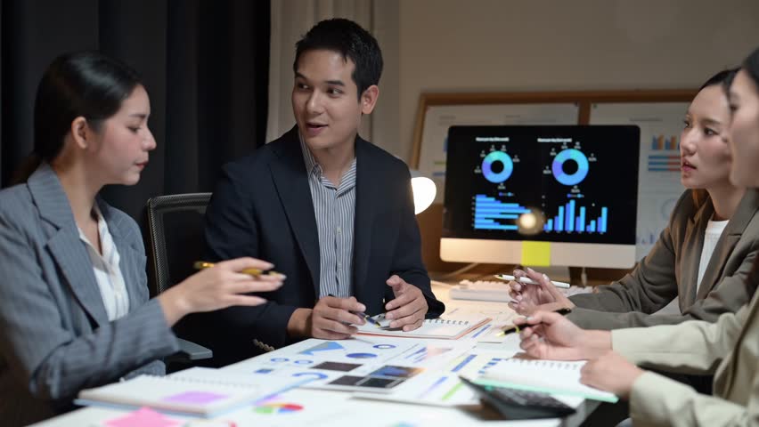 A group of people are sitting around a table with a computer monitor in front of them. There are two men and two women in the group