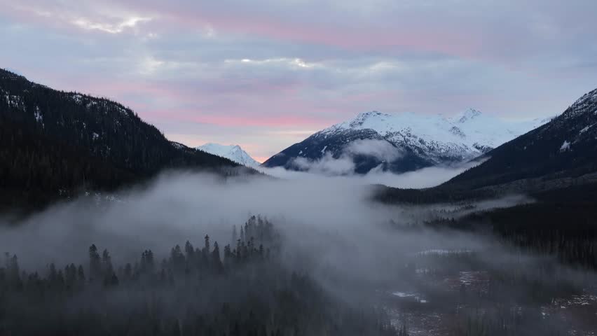 Majestic Winter Landscape: Fog Rolls Through a Valley with Snow-Capped Mountains at Dawn in British Columbia, Canada