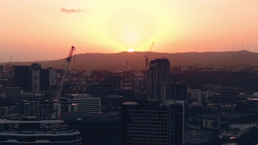 Aerial descend across Brisbane skyline from Teneriffe as dusk colors settle over city with tall construction cranes, CBD Queensland Australia