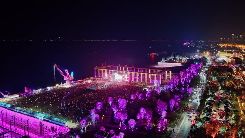 Aerial night view of music festival stage lights fans crowd in excitement.   Scene at outdoor concert with people dancing enjoying live performance in fest.