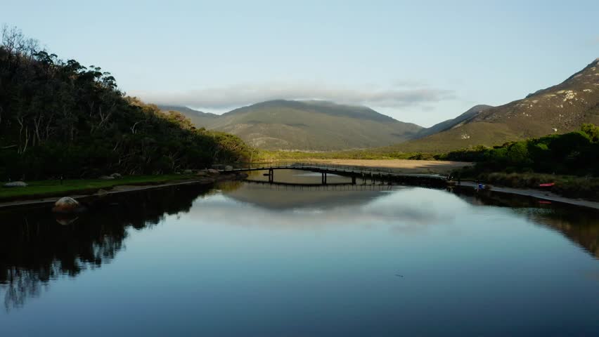 Drone dolly a quiet coastal inlet with reflective water framed by hills and natural shoreline, flyover bridge and reflection, Victoria Australia