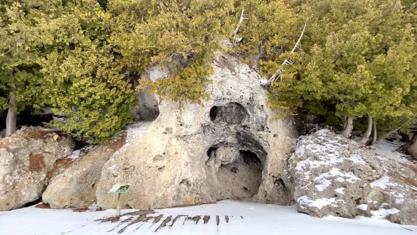 Natural rock cave formation on a snowy trail surrounded by evergreen trees