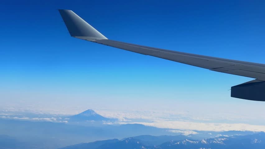 Plane wing and Mount Fuji seen from an airplane on a beautiful blue day with snow on the peak.