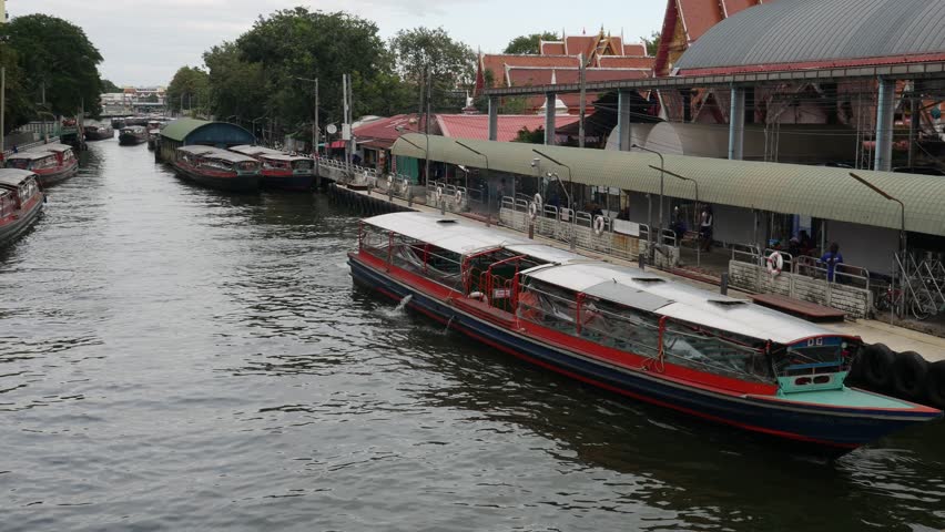Passenger boat moving on canal water in city with green trees and flowers on bank, public water transportation system and commuting travel.