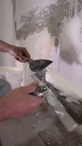 A close-up shot of a person applying white plaster to a wall with a spatula, carefully spreading the mixture to cover imperfections