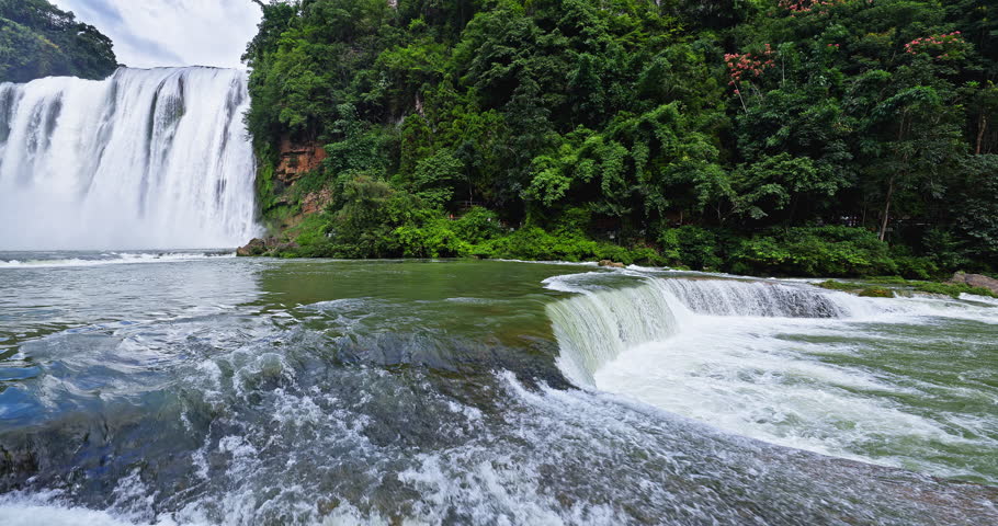 Huangguoshu Waterfall natural landscape in Guizhou Province, China. A magnificent waterfall and turbulent river flowing over rocks, set within lush green forest landscape.