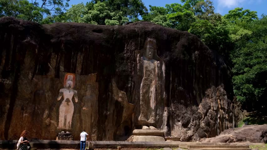 Ancient Buduruwagala rock carvings carved into a cliff in Sri Lanka. Large standing Buddha statues surrounded by tropical greenery, Sacred Buddhist heritage site, spiritual atmosphere and history.