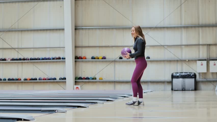 Slow motion side view of sporty woman throwing bowling ball spacious bright hall